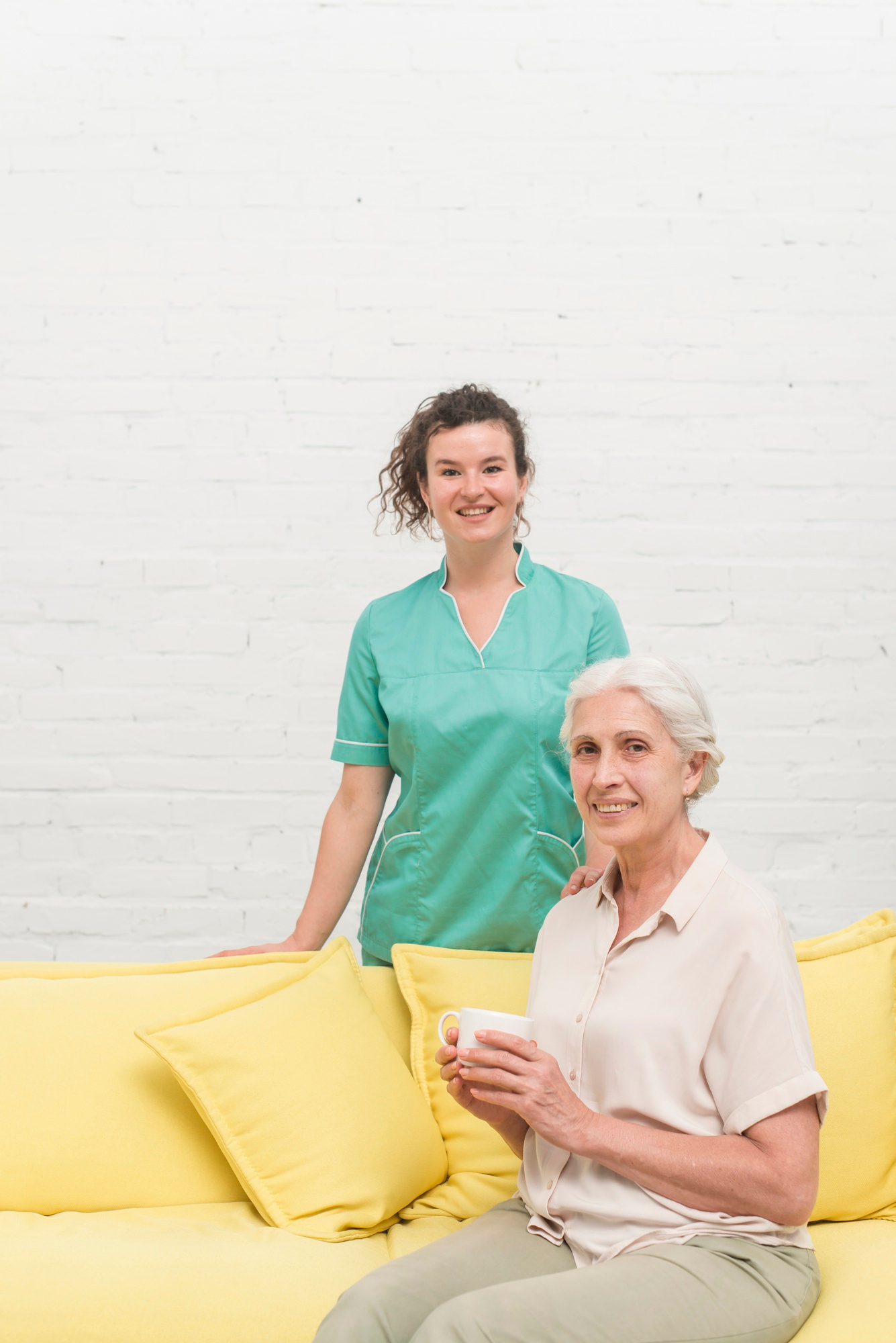 smiling-senior-woman-sitting-sofa-holding-coffee-cup-front-nurse